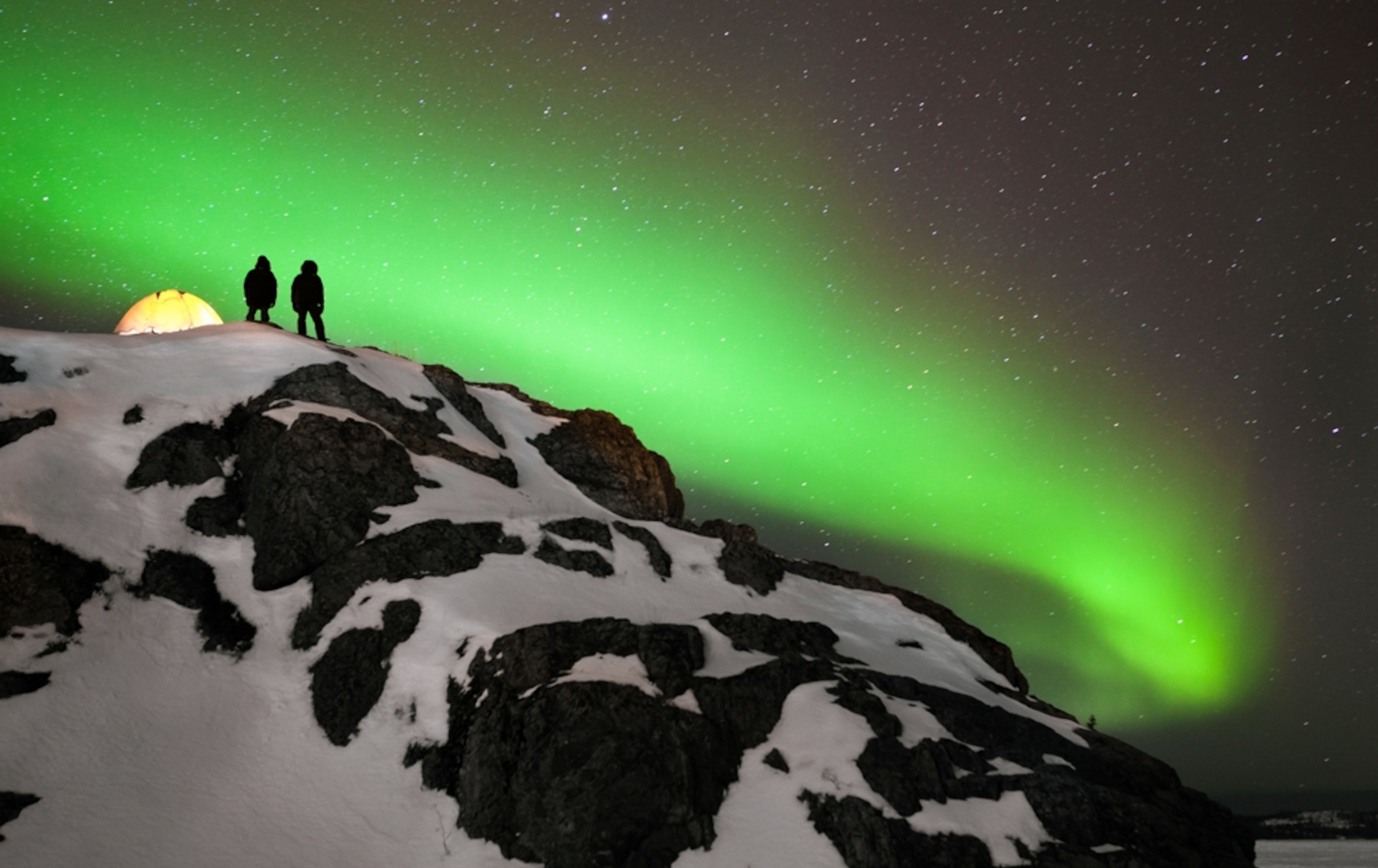 Aurora picture: people looking at the northern lights from a snowy hill