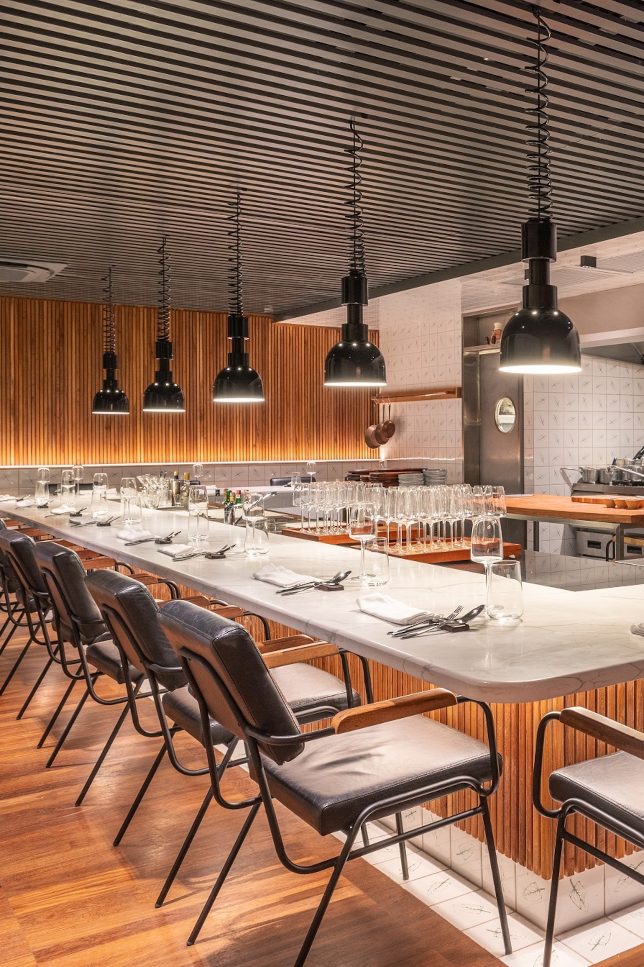 The interior of a modern restaurant with bar seating around a kitchen.