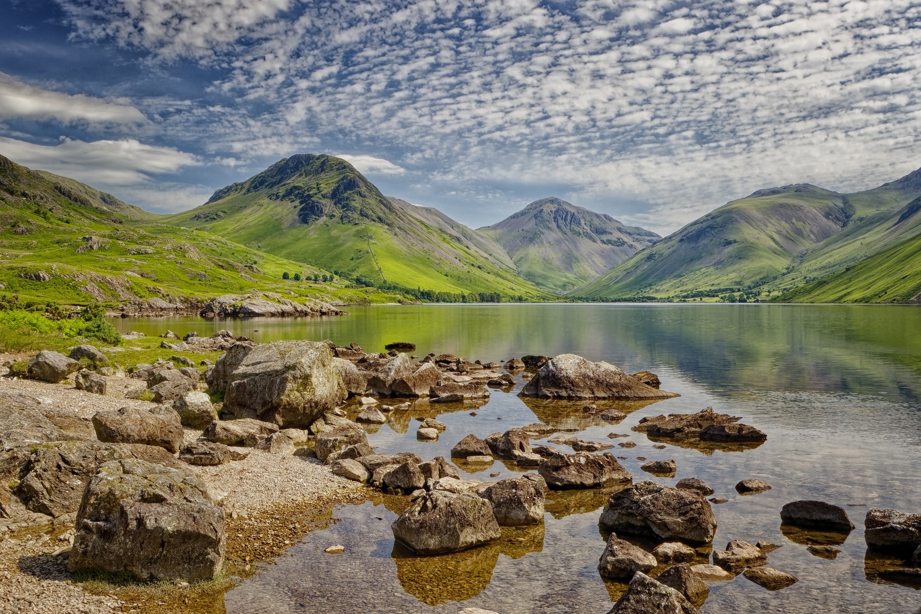 The shores of a mountain lake with a range in the background and boulders marking the shore.