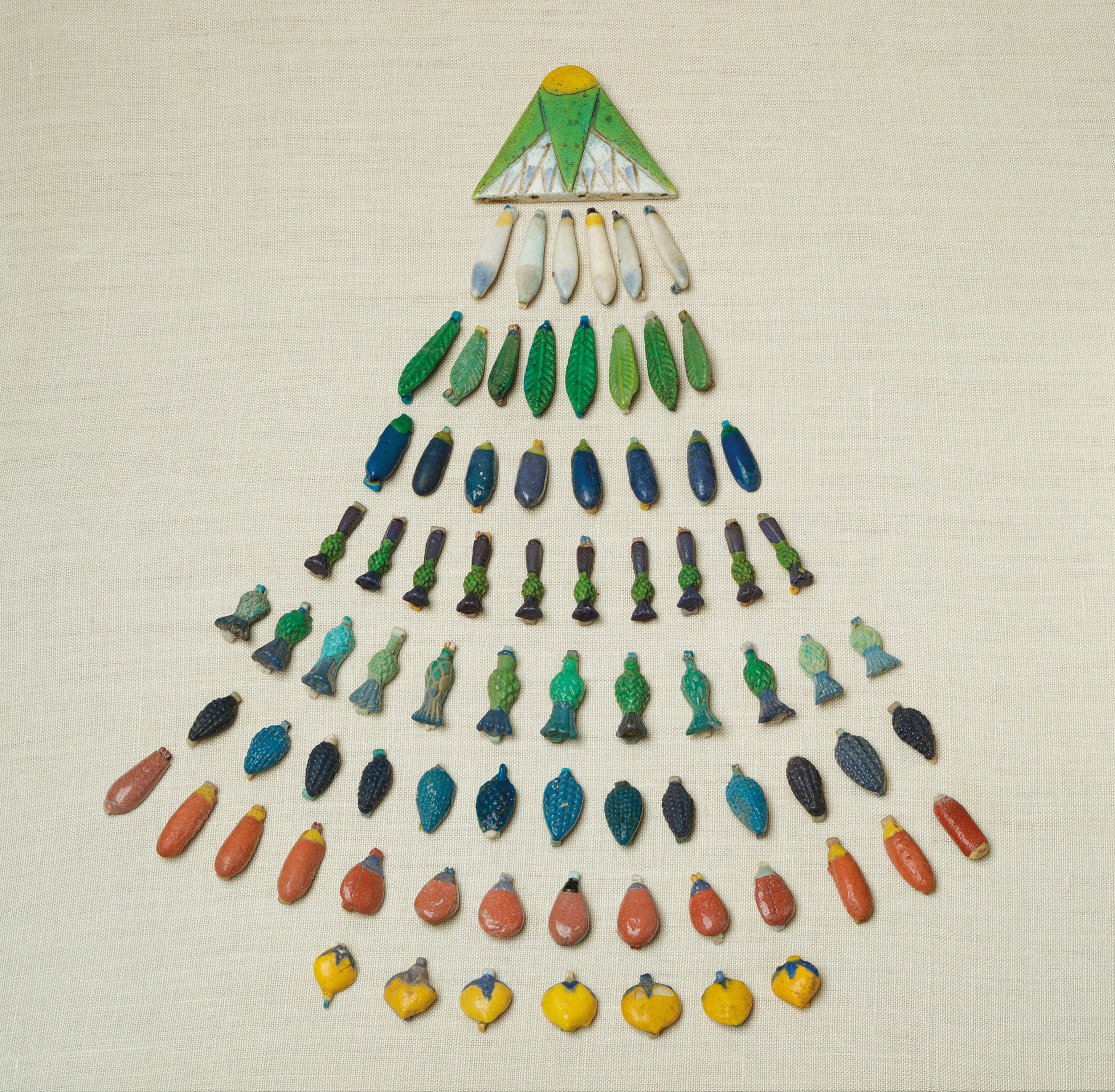 Egyptian beads laid out in the shape of leaves, petals and fruits for a broad collar.