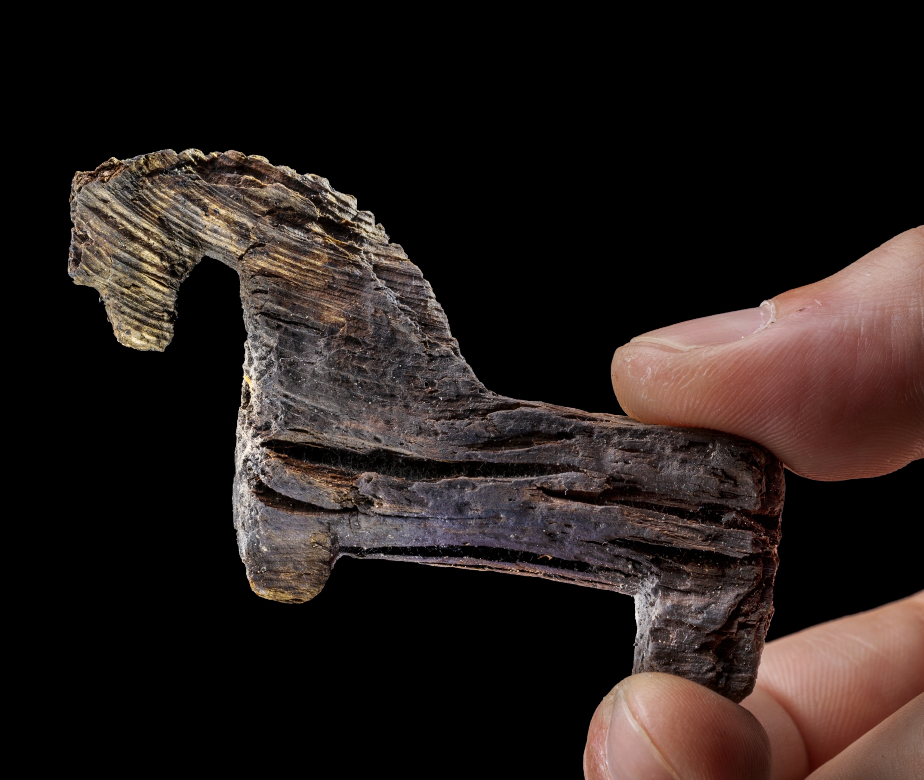 Little figurine of horse held between two human fingers.