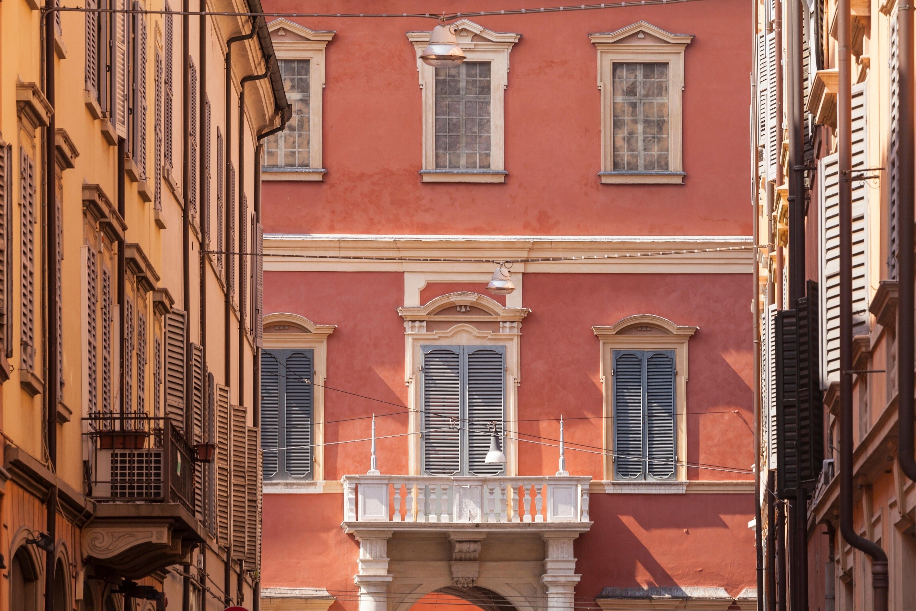 A red building in the centre of Modena. It has a white balcony.