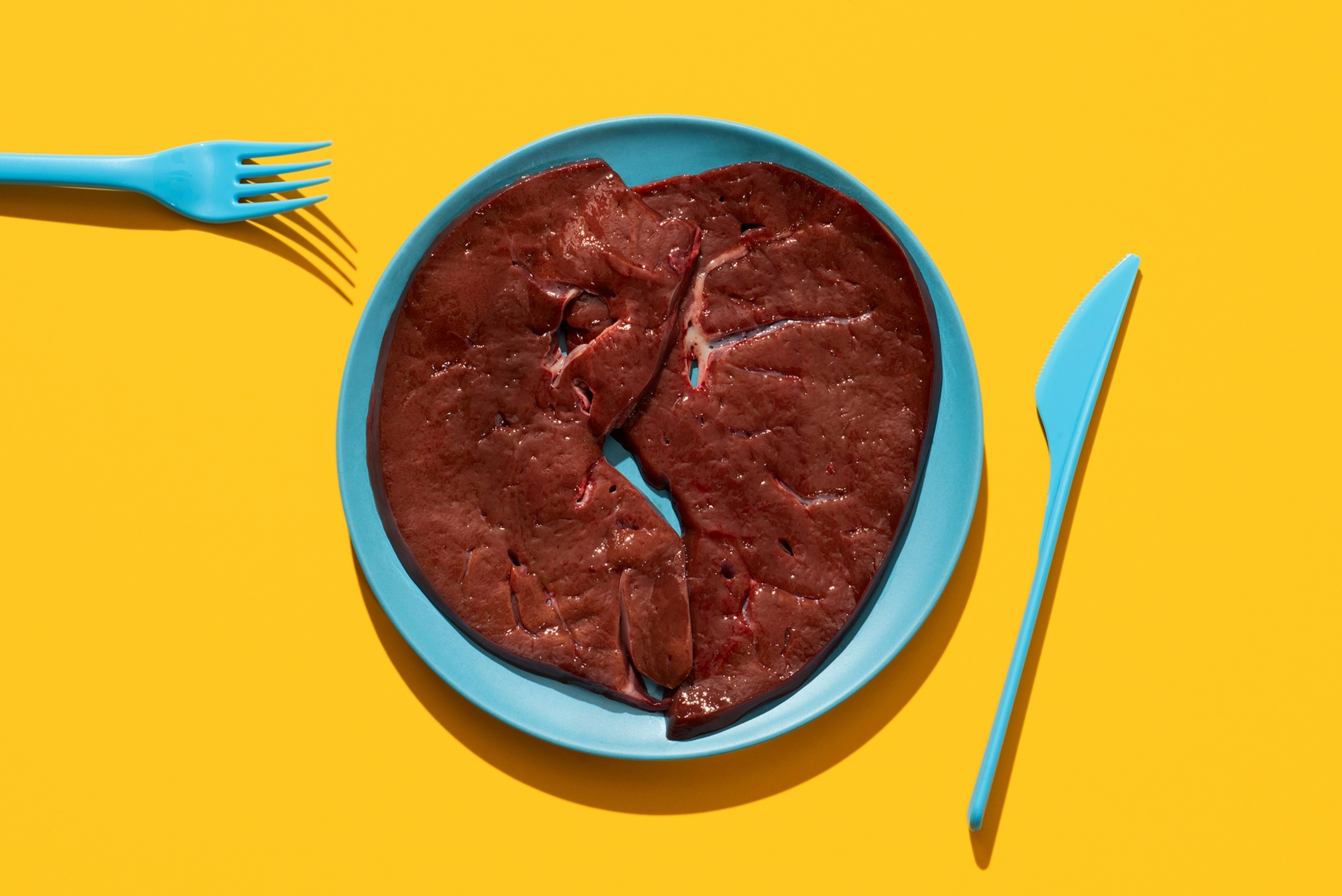 some slices of raw beef liver in a plate, on a yellow background