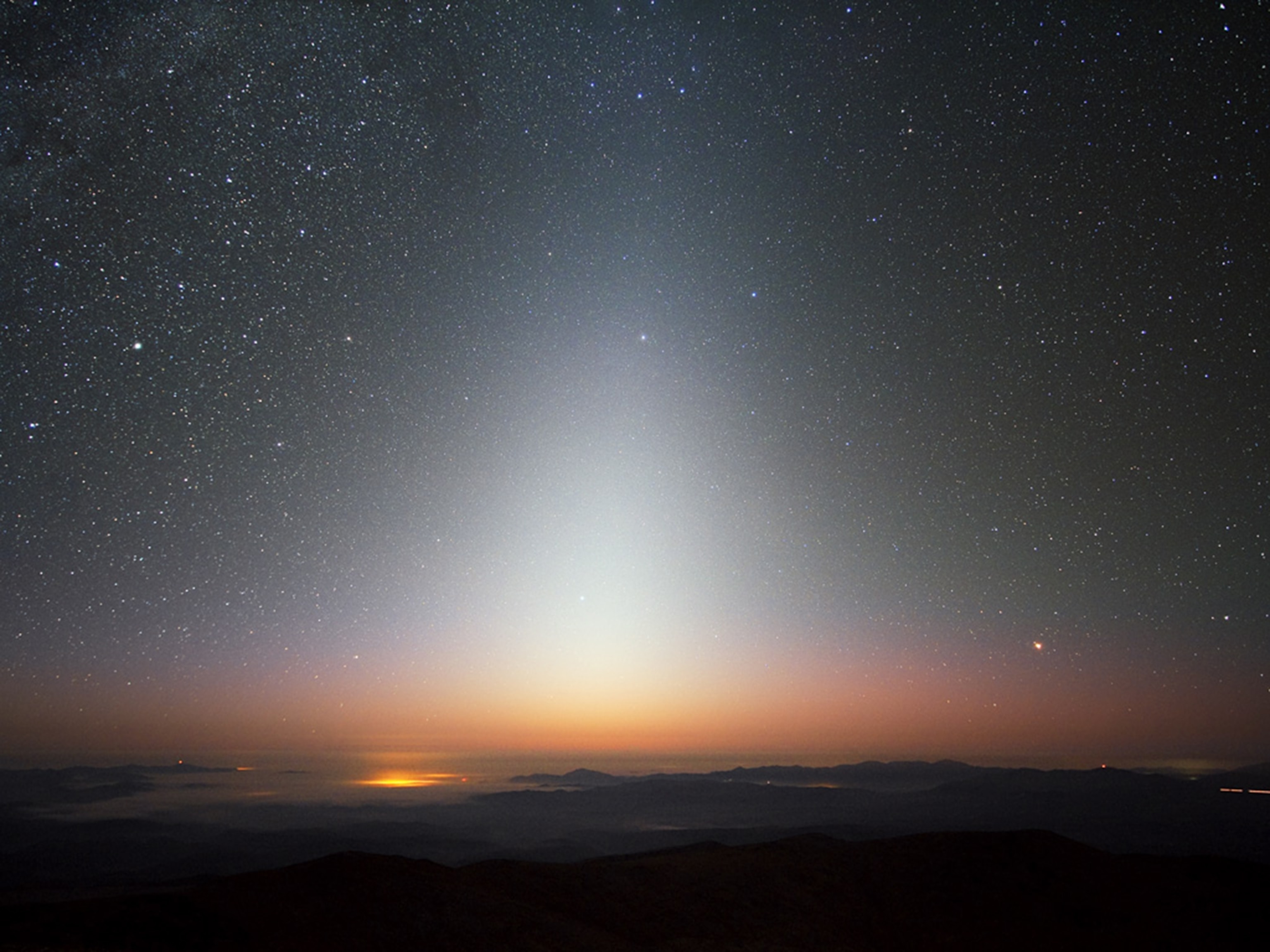 An artist’s view from an imagined planet around a nearby star shows the brilliant glow of exozodiacal light extending up into the sky and swamping the Milky Way