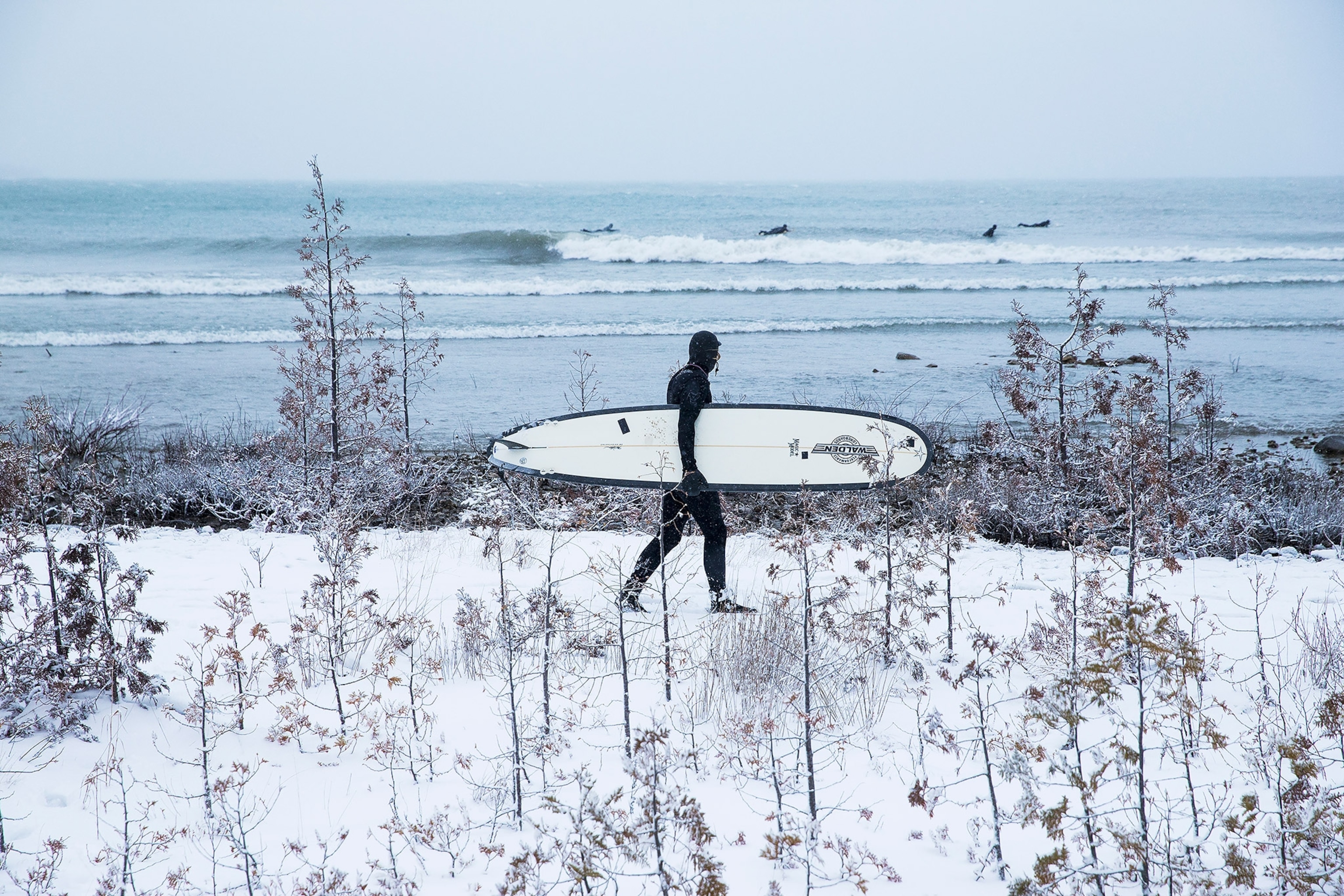 a person in a wet suit holding a surfboard and walking away from Lake Huron in Michigan