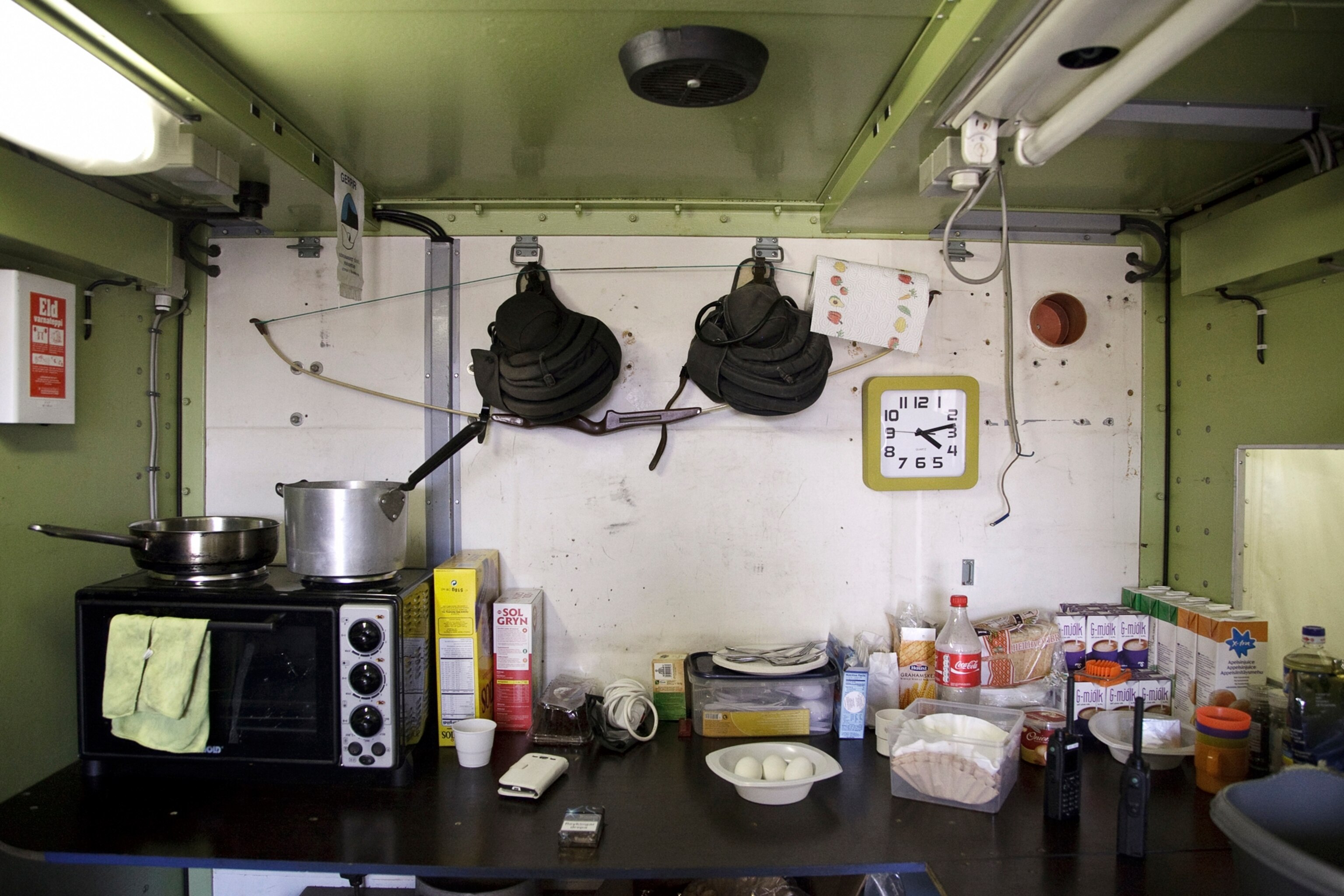 the interior of the Civil Protection checkpoint, two helmets and a bow hang on the wall over a counter with kitchen supplies