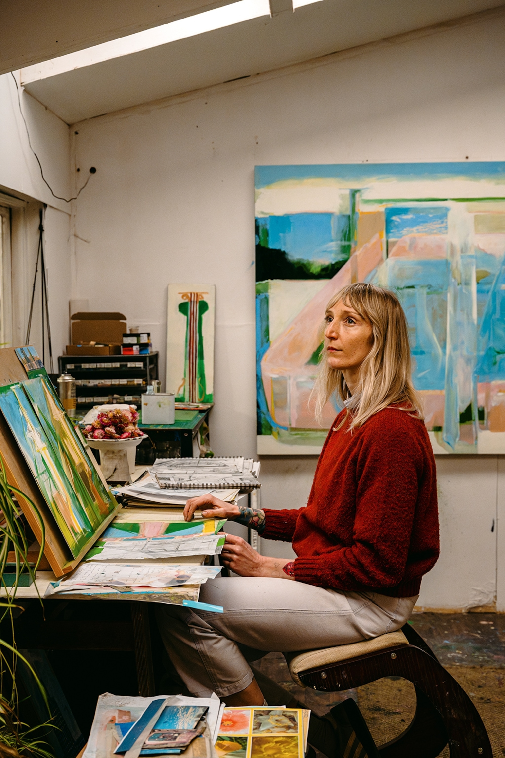 A young female artist sat in front of her workbench in her studio.