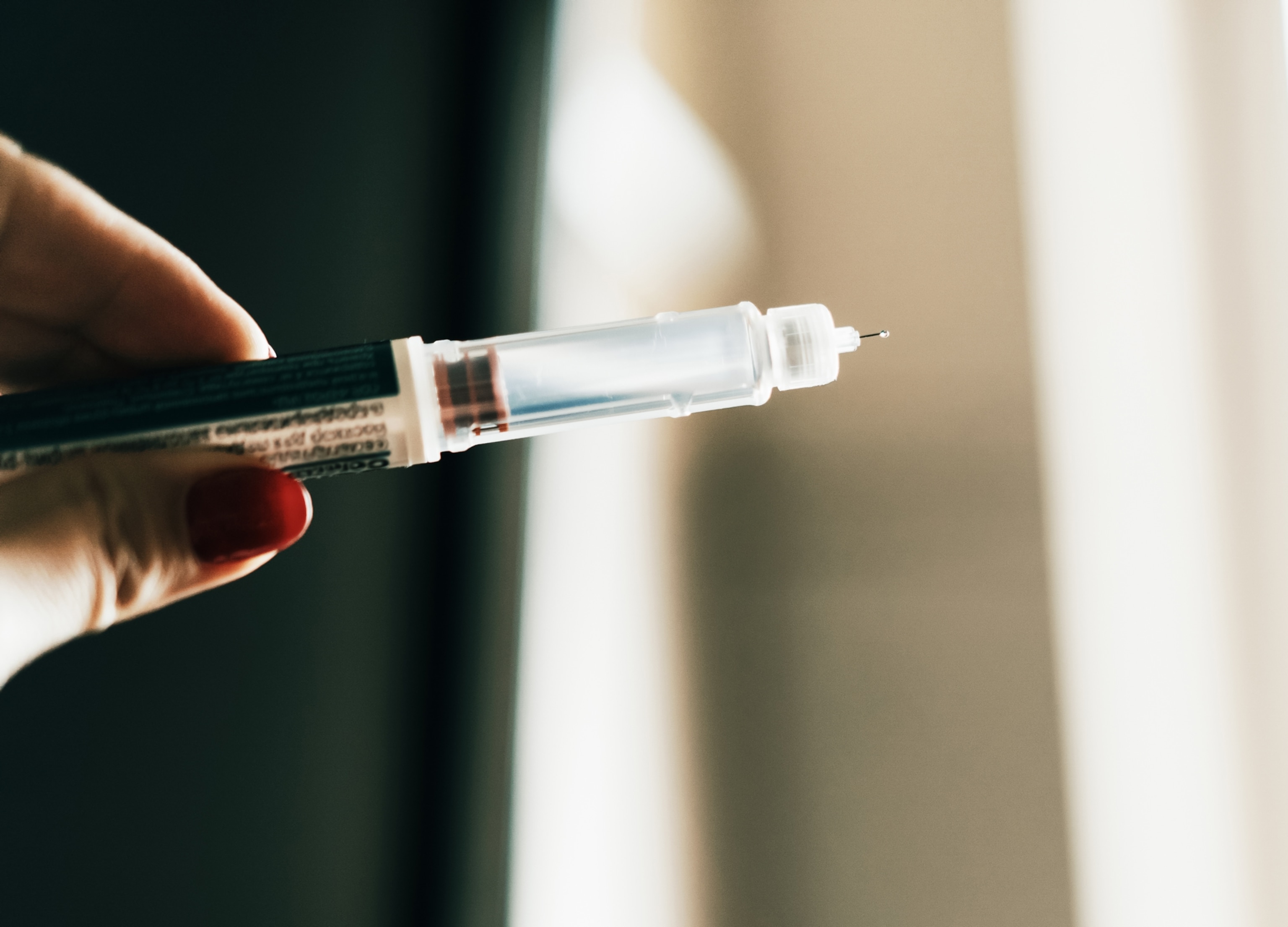 A detailed view of a syringe device being held in a hand, ready for use.