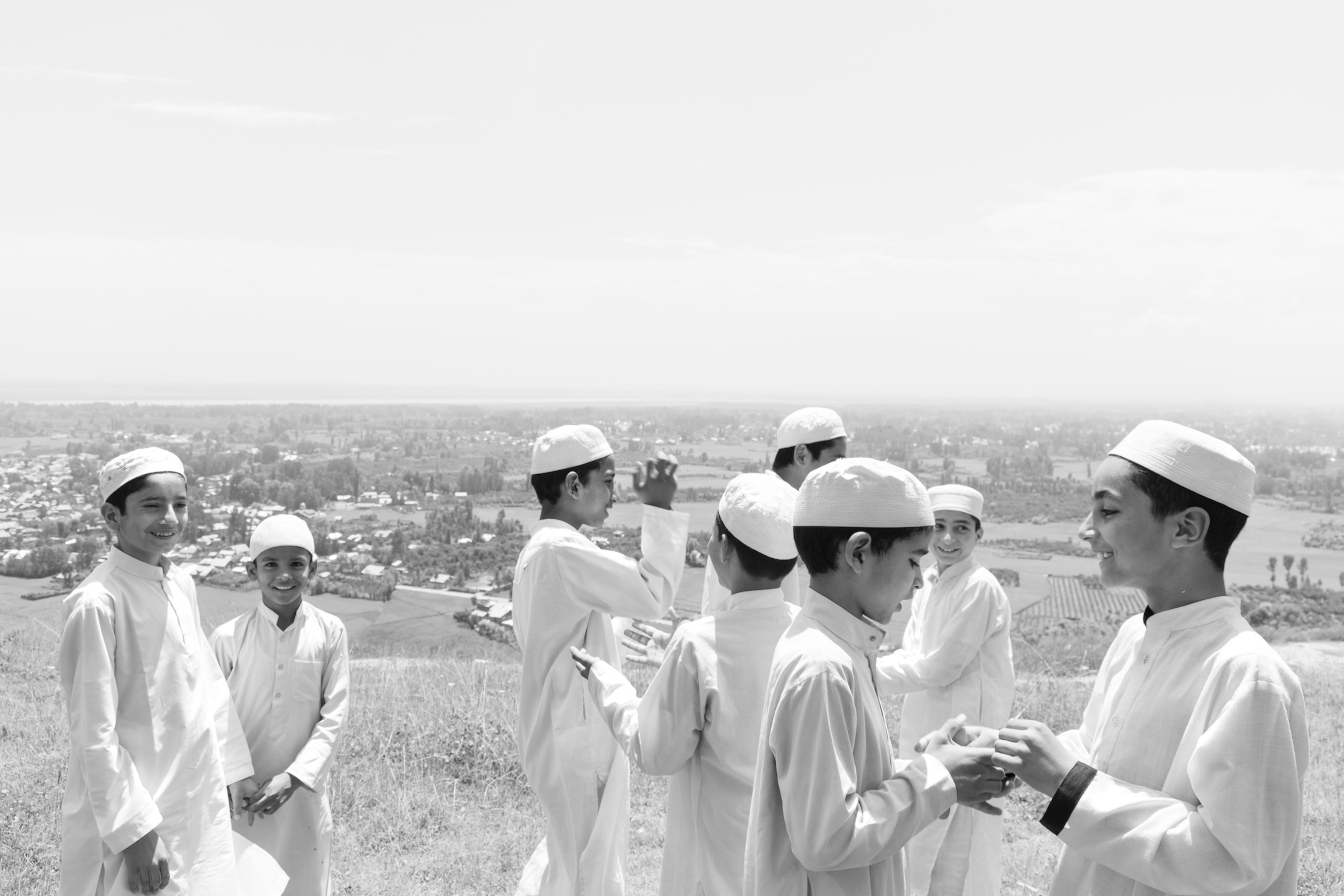 A black and white photo of a group of young boys playing on a hill, all of them wearing traditional Islamic caps.