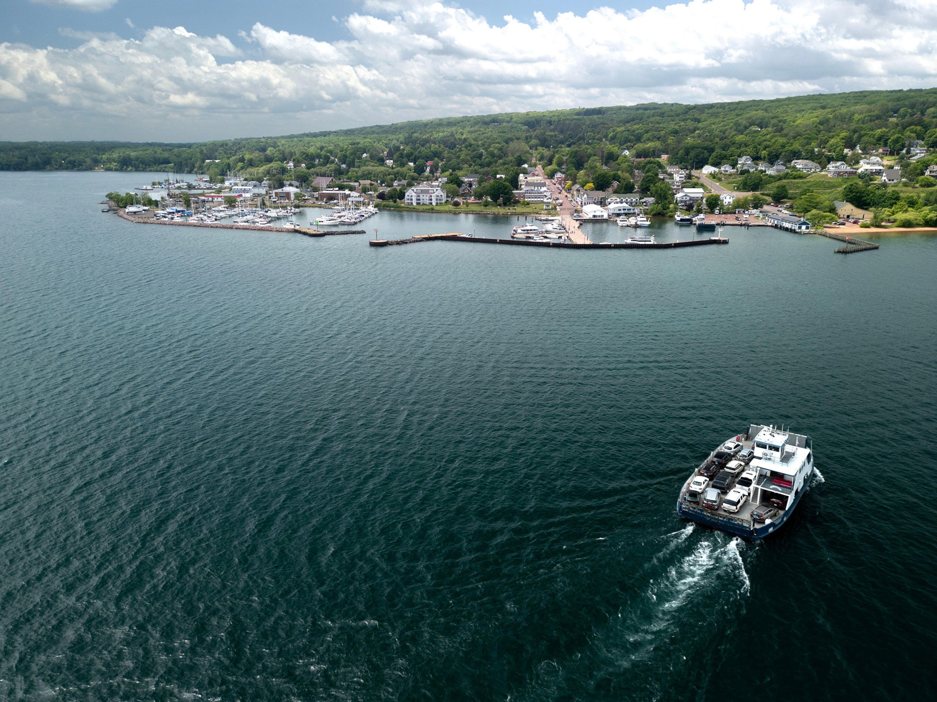 A ferry moves across a blue lake toward a small town on a shoreline