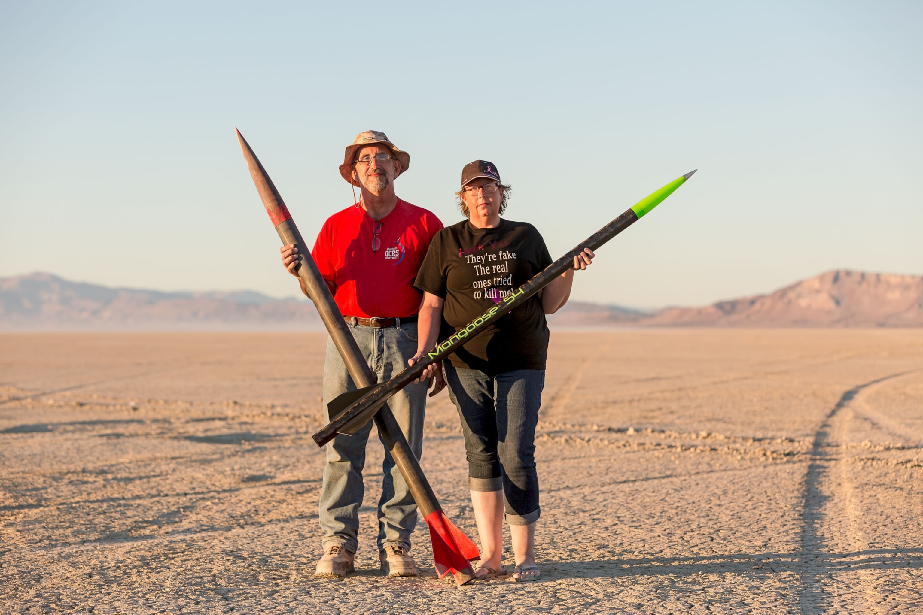 a man and woman standing the desert each holding their own rocket