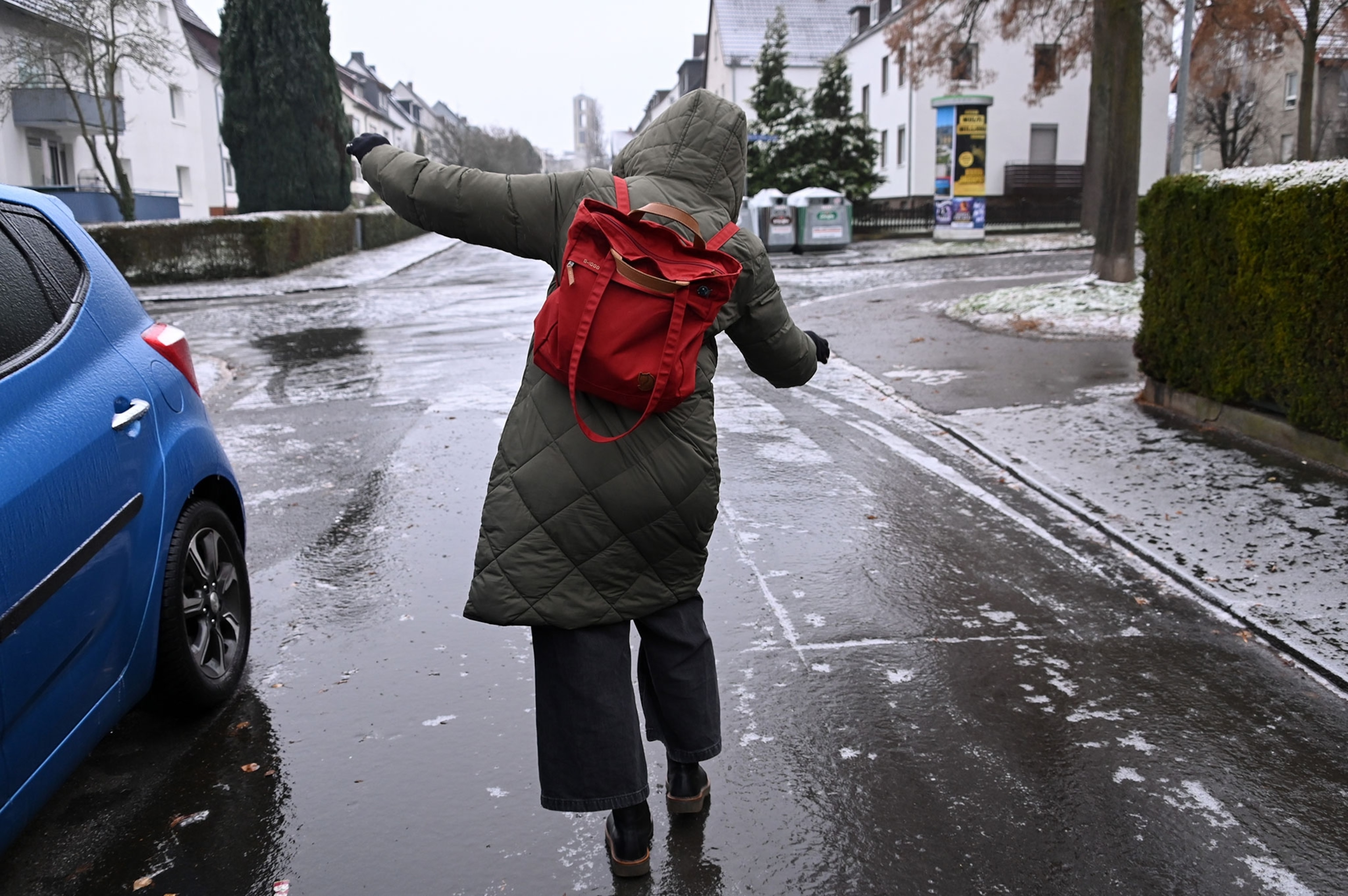 A woman stretches her arms out as she walks, the road is reflecting light.