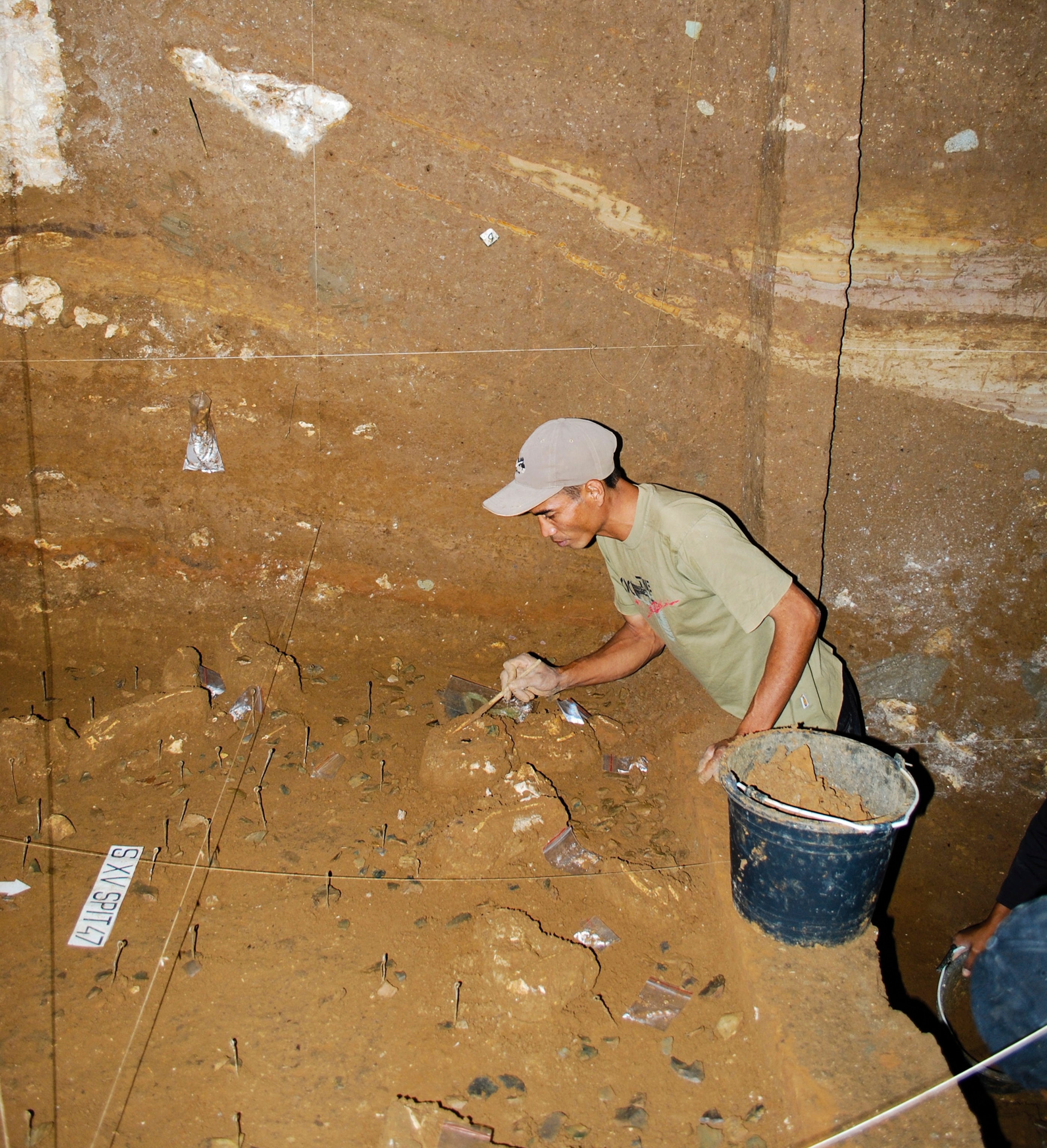 A man wearing a ball cap carefully examines an archaeological excavation.