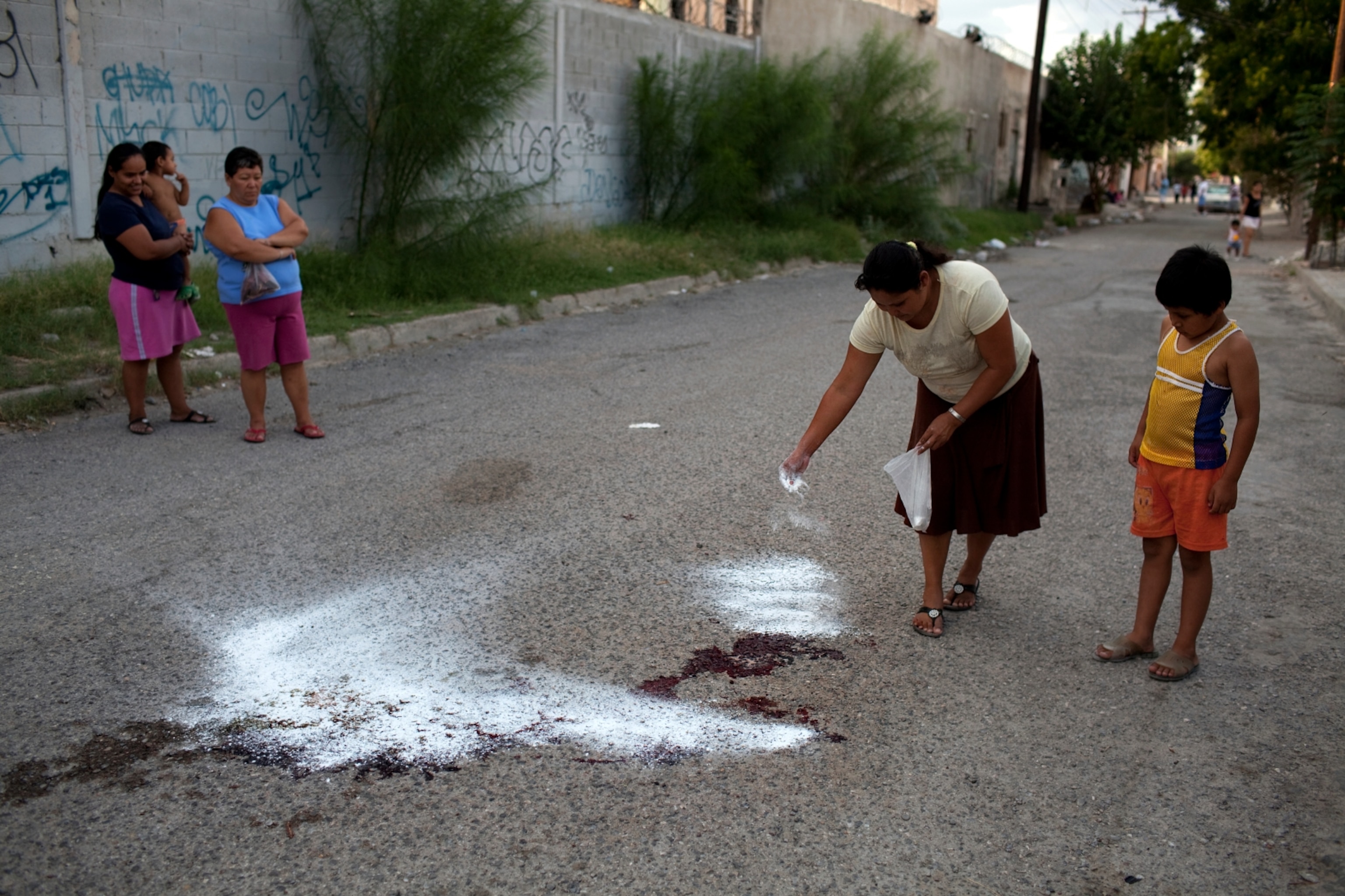 A women puts down flour to soak up blood on the pavement where a young man was murdered August 6, 2009, in Ciudad Juarez.