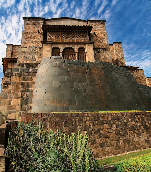 The Convent of Santo Domingo in Cusco sits on a green hill with a blue sky