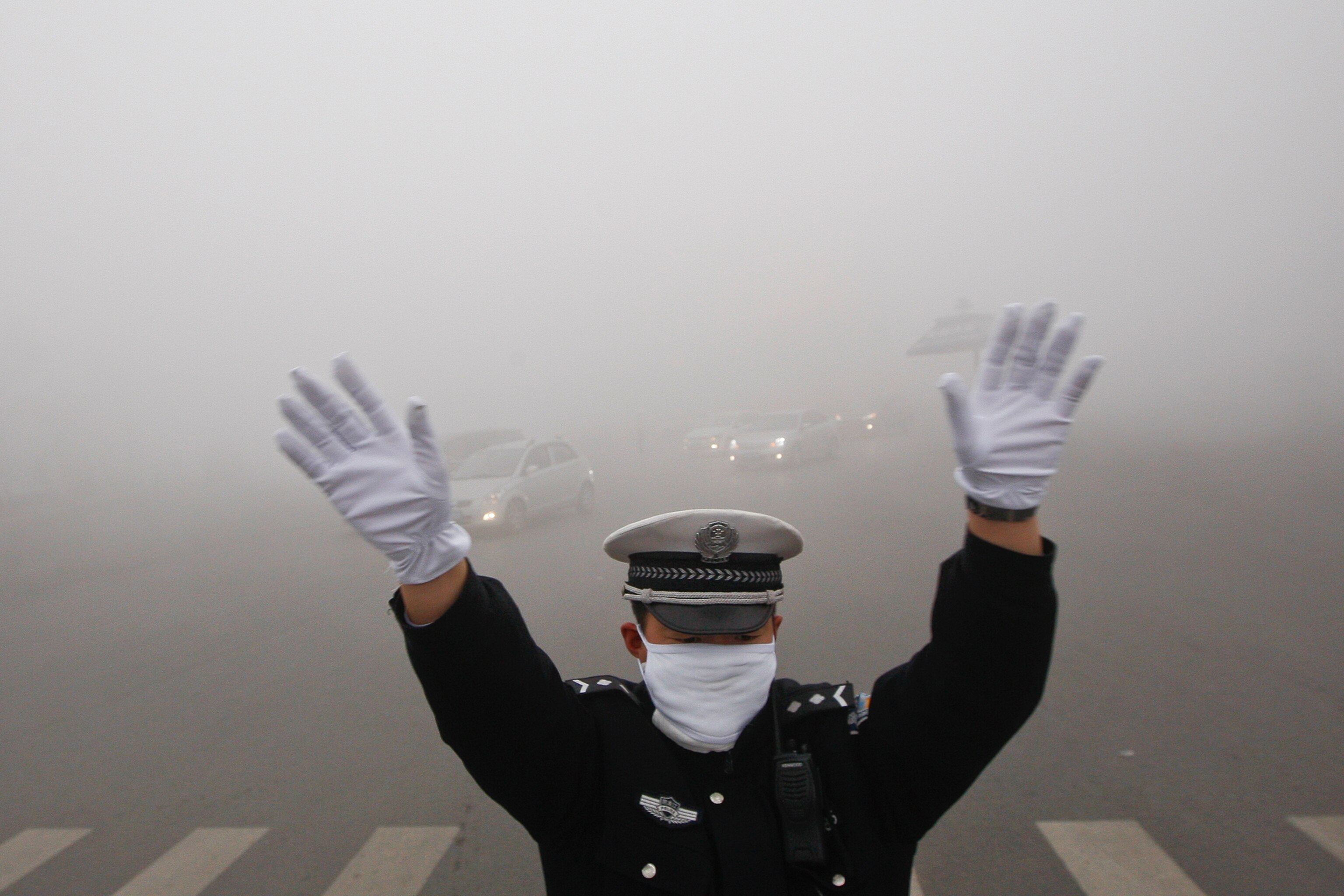 a traffic policeman signaling to drivers during a smoggy day in Harbin, China.