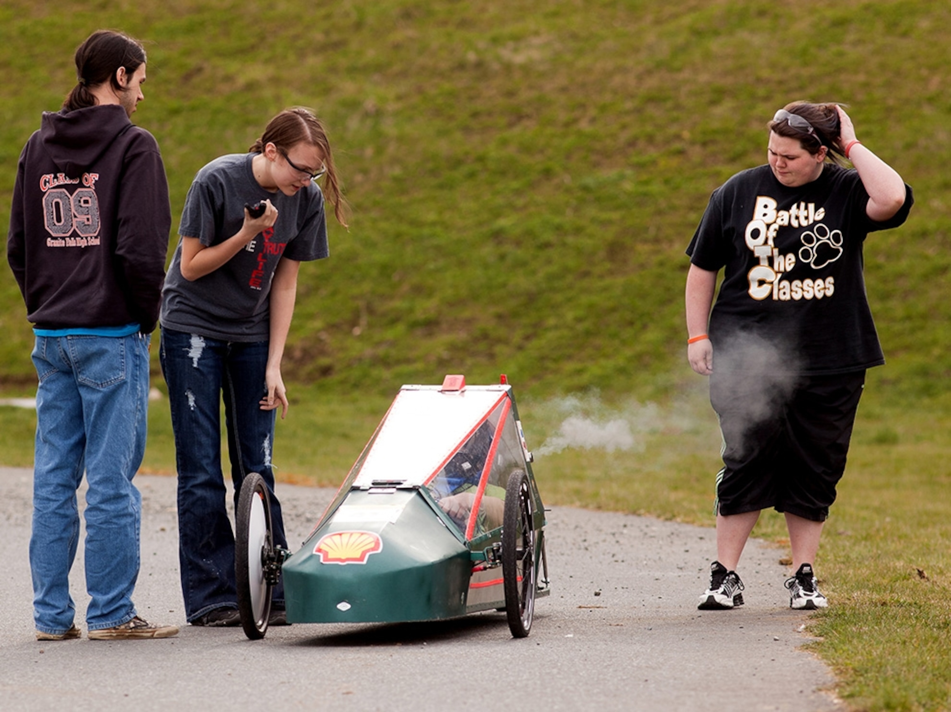 Students talk with a teammate as she sits in the driver’s seat of a car