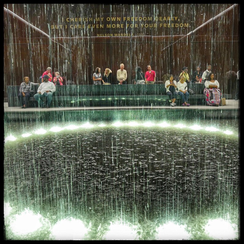 Museumgoers sit around a circle of water in the Contemplative Court at the end of their tour of the museum.