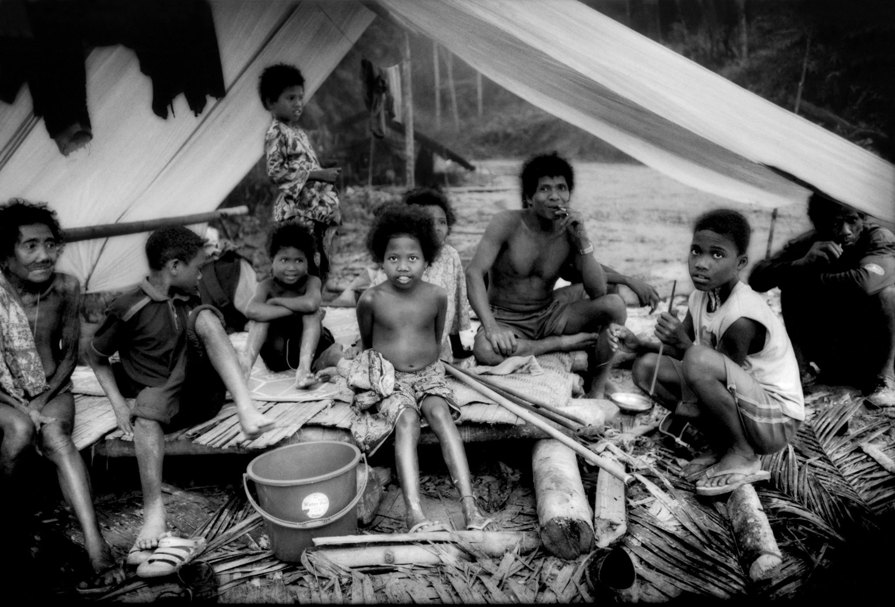 a Batek Negrito family sheltering from the rain in a typical structure