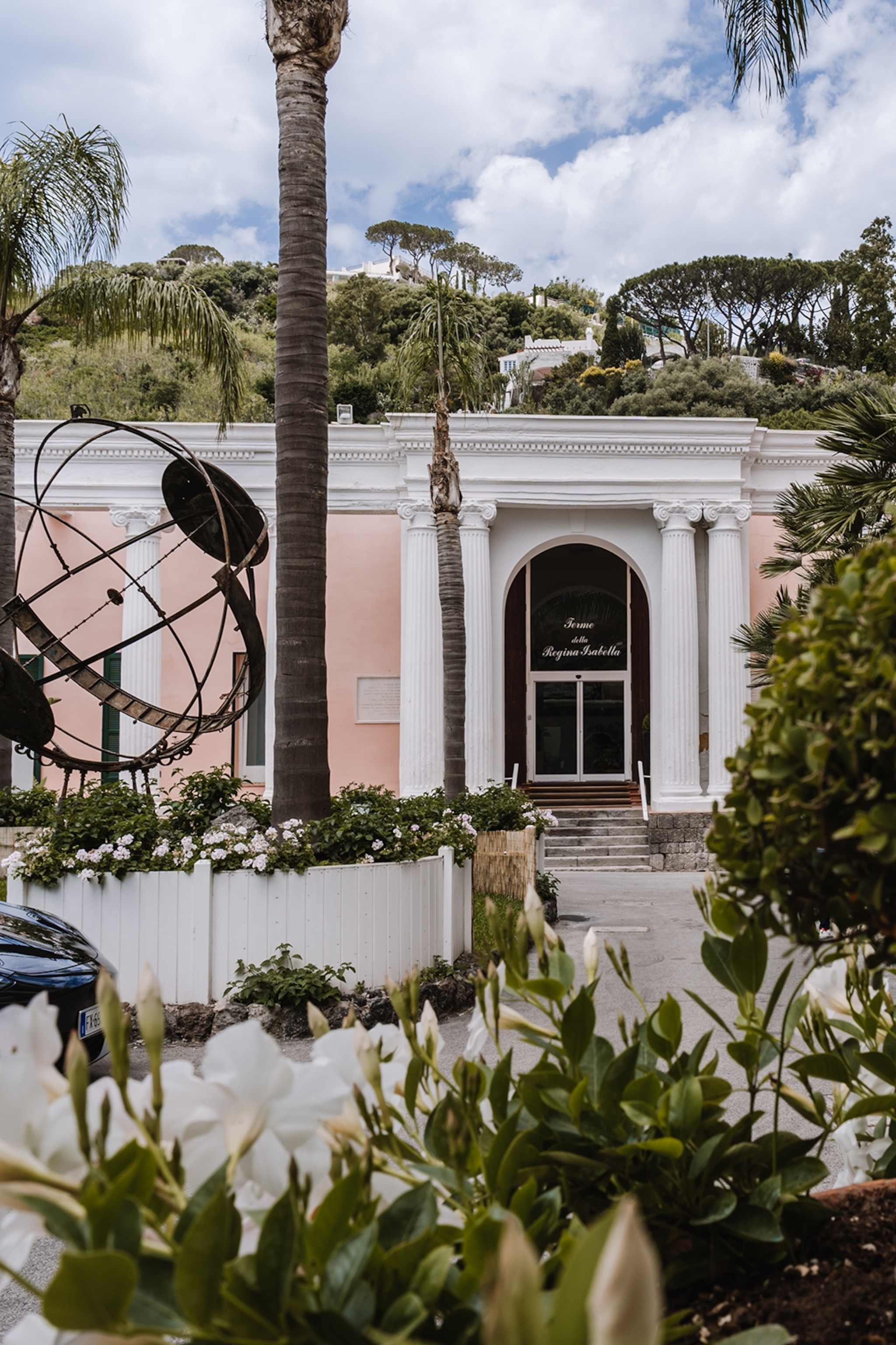 The entrance of a spa hotel with cursive lettering and a bronze globe sculpture outside.