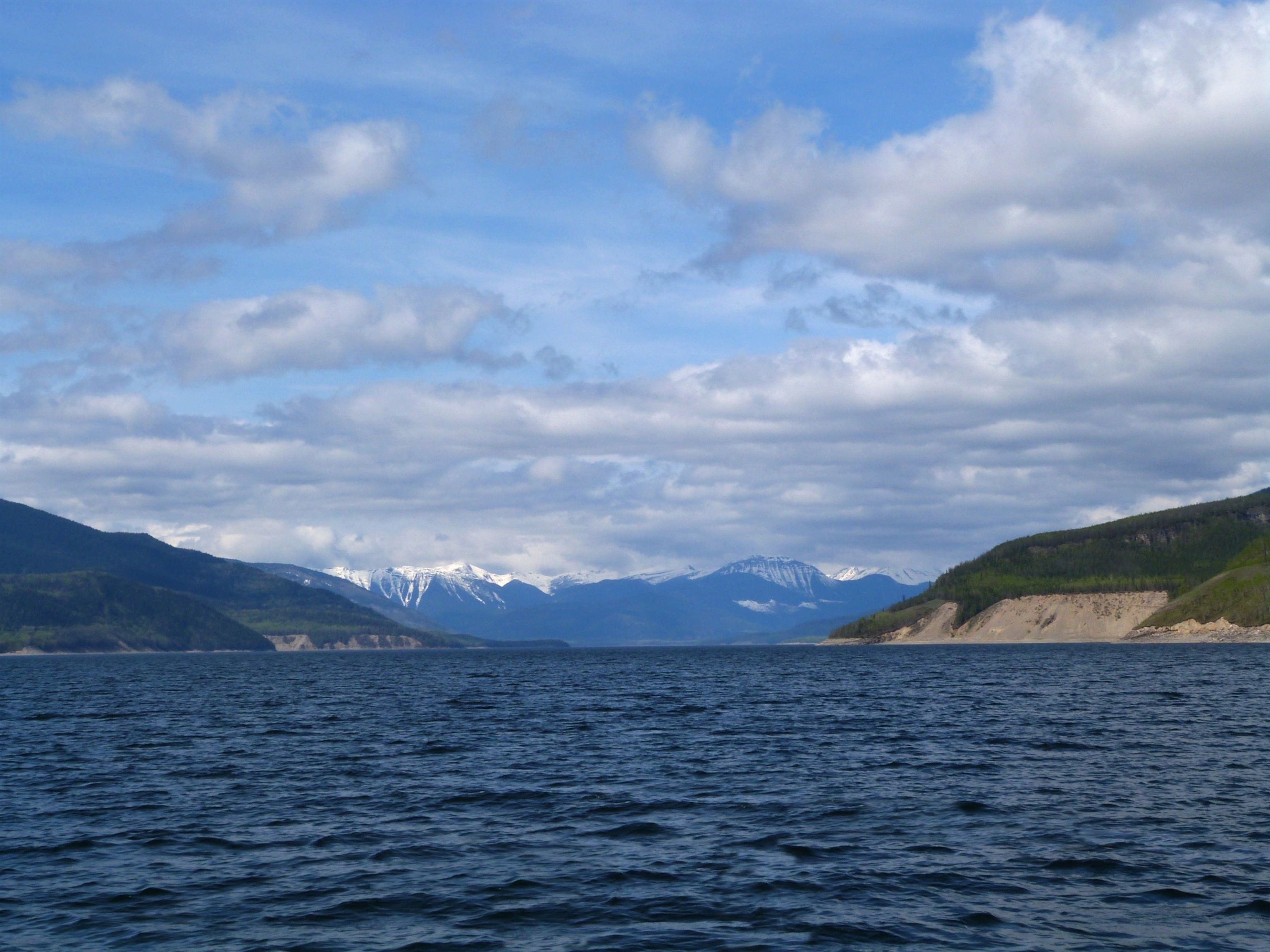 Distant snowcapped mountain range and gentle cloudscape from an off-shore view of Williston Lake, British Columbia, Canada.