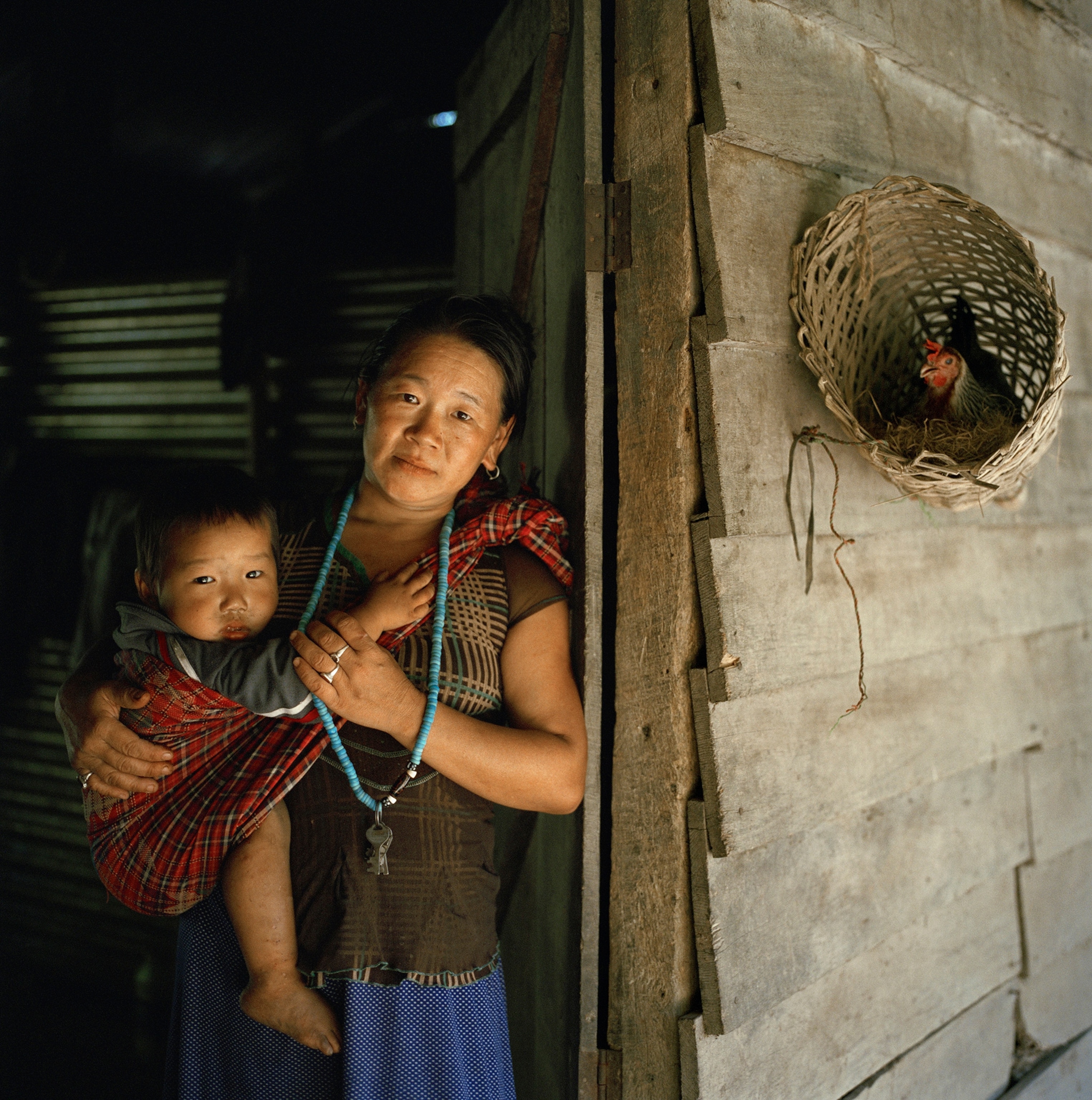 A woman stands in a doorway with her toddler son strapped to her side.