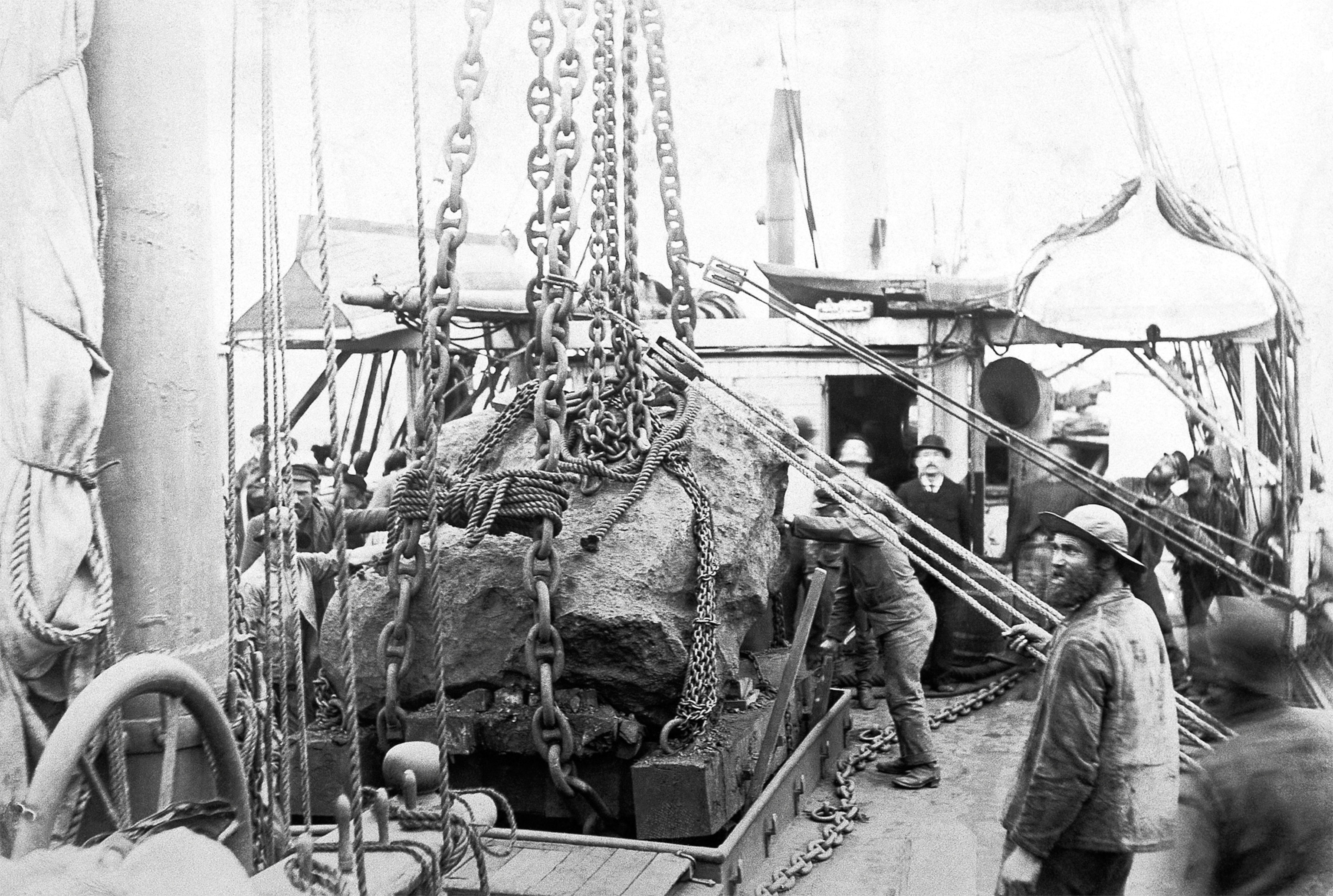 a meteorite being loaded onto a ship with ropes and chains