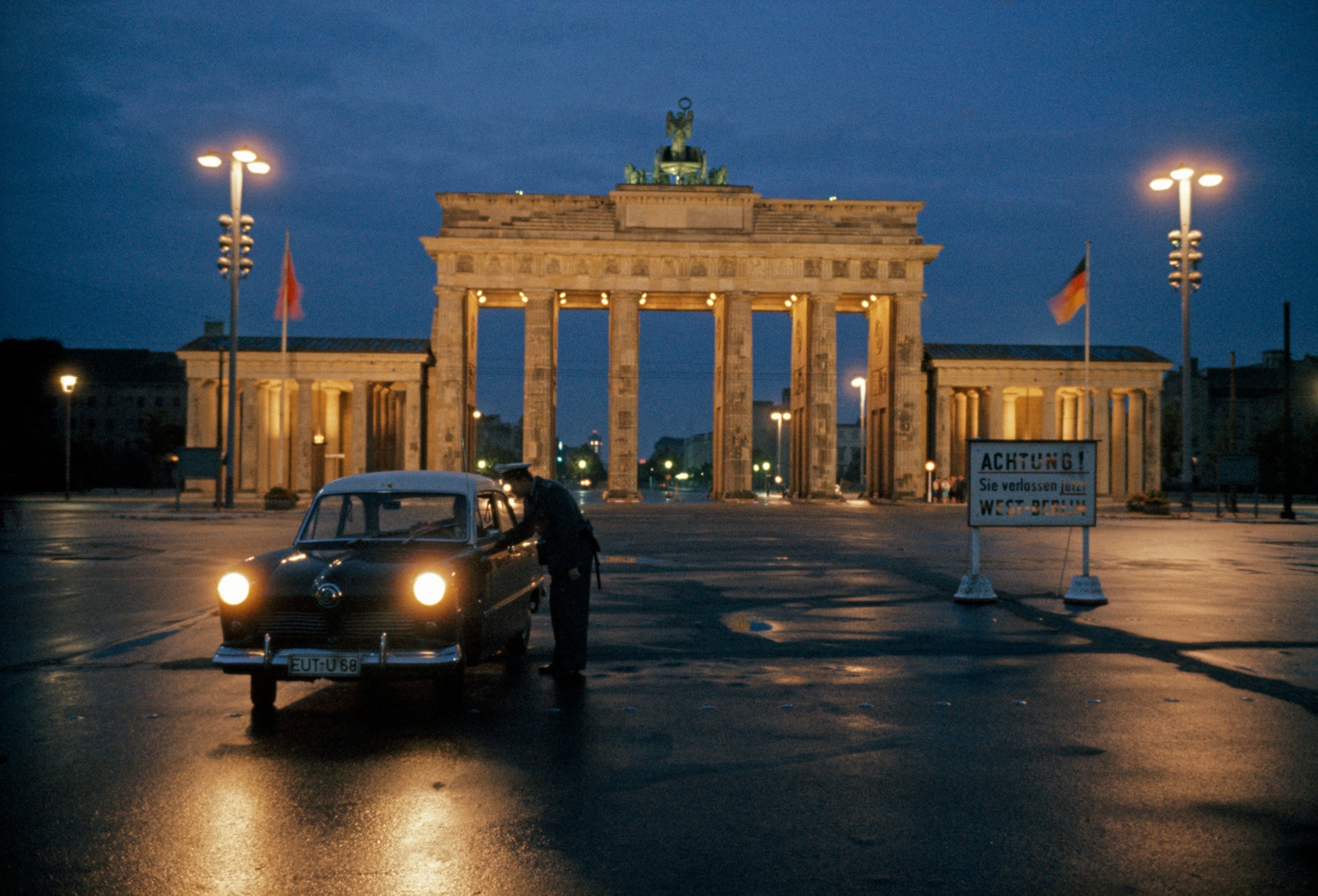 Divided Berlin lies 104 miles inside Communist Germany, but the United States, Great Britain, and France guarantee the freedom of the Western sectors. The great gate, builtin 1788-91 under King Frederick William II of Prussia, stands just inside East Berlin. Russian and East German flags flank the gate. "Attention! You are now leaving West Berlin," warns the sign in this picture, taken on the eve of the border closing.