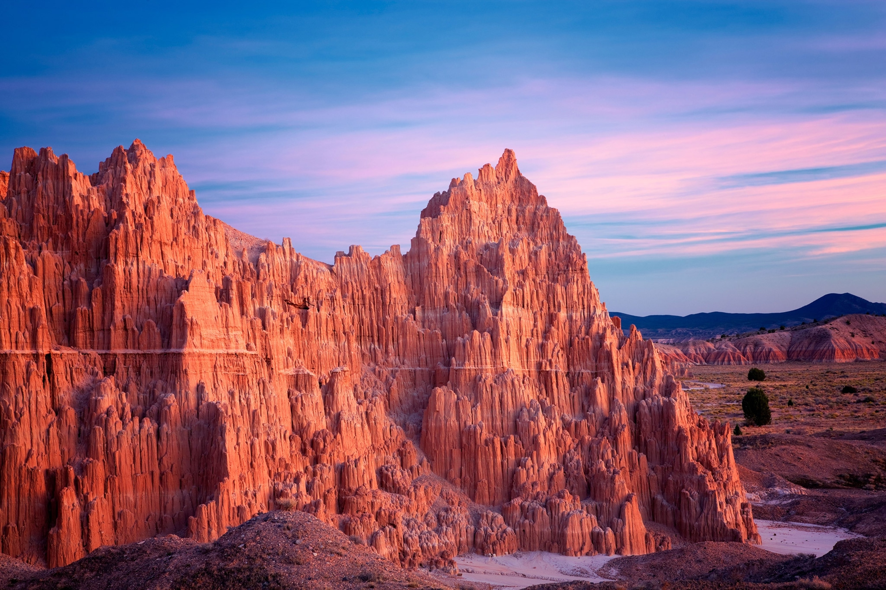A spiky, towering red rock formation beneath a pink and blue sunset sky