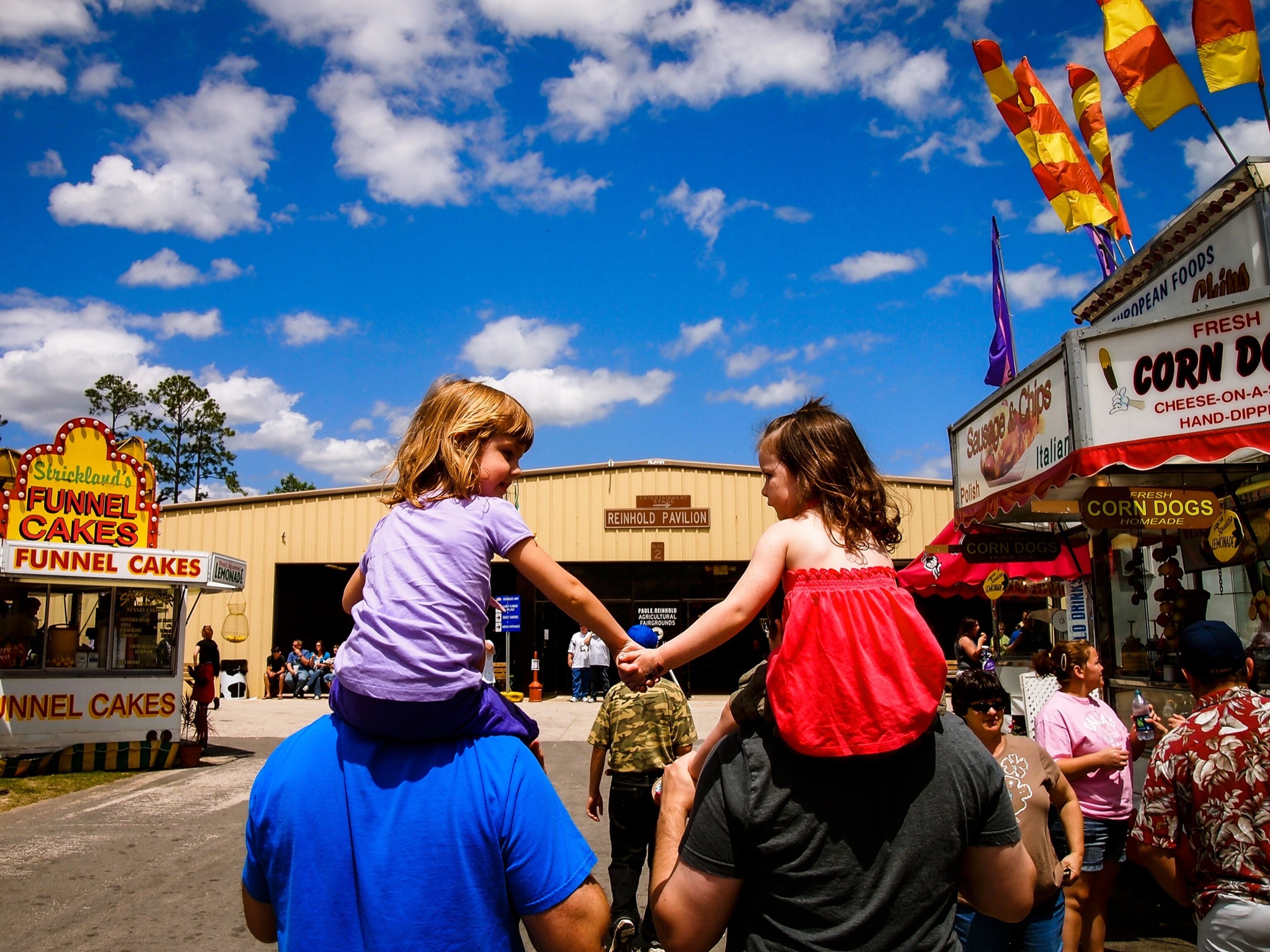 two shoulder-seated children holding hands