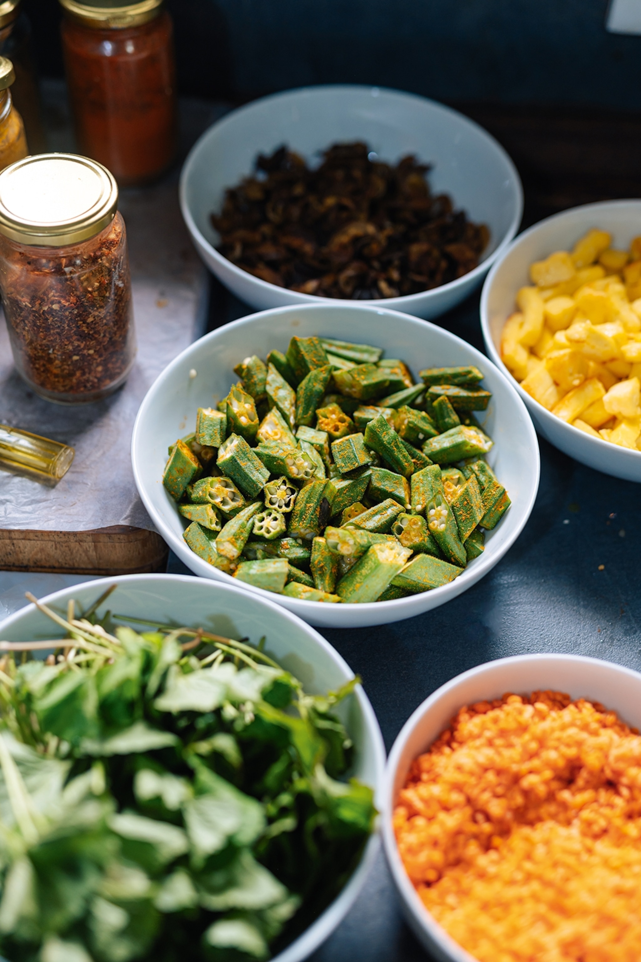 A simple arrangement of dishes in bowls, including spiced and fried okra, red lentil dal and chilli oil in a jar.
