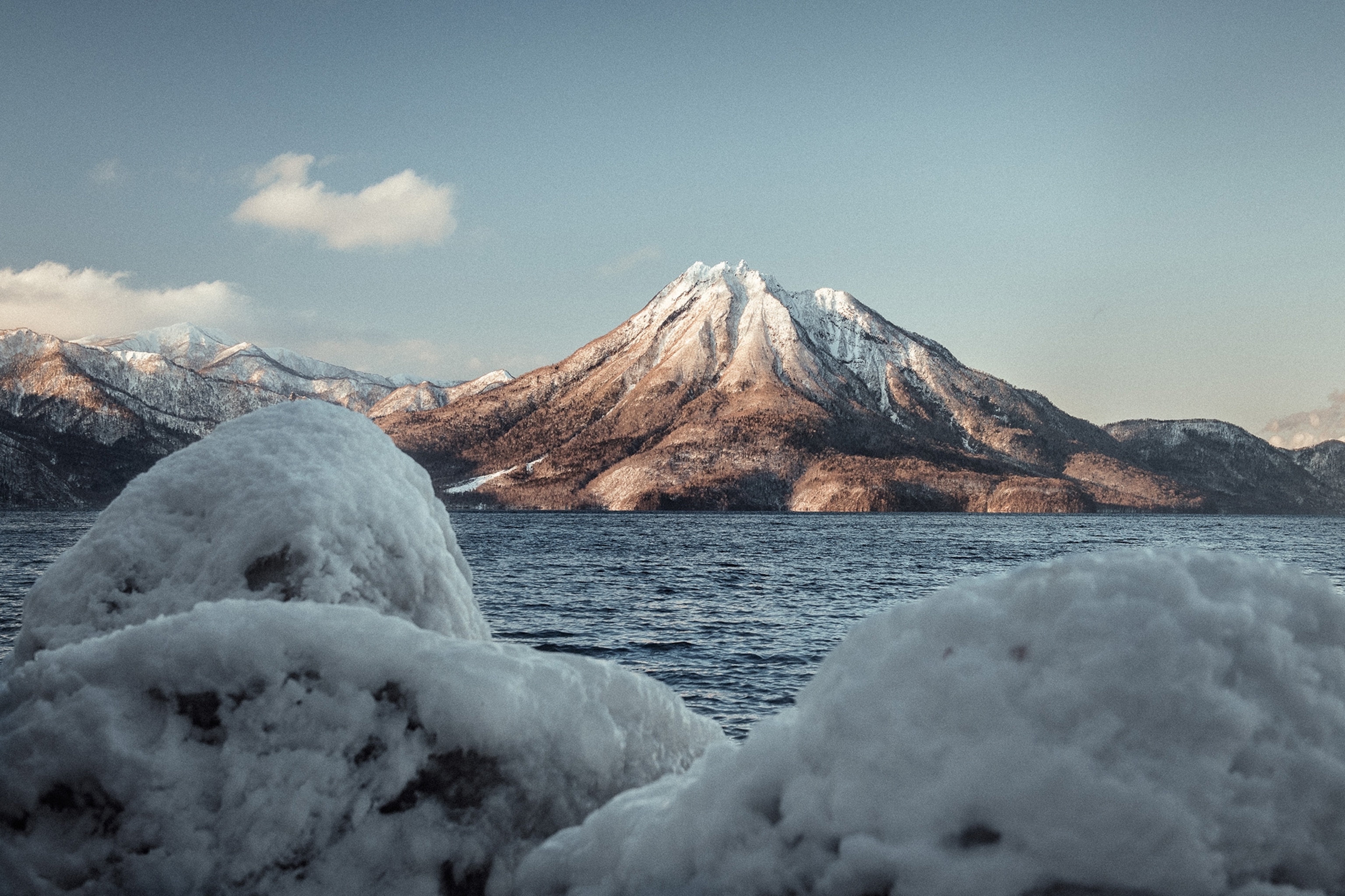 A calm sea at the edge of a snow-peaked mountain with a low ice wall framing the view.